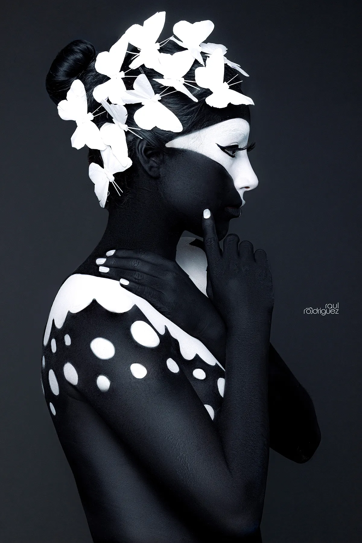 Retrato de perfil con mariposas blancas en el cabello, una mano sobre el hombro y un dedo apoyado en la mejilla.